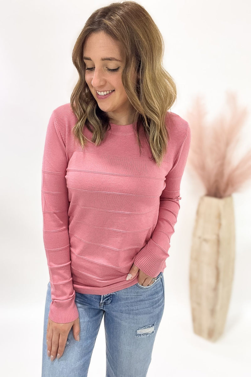 Woman wearing a pink long-sleeve top and blue jeans on a white background