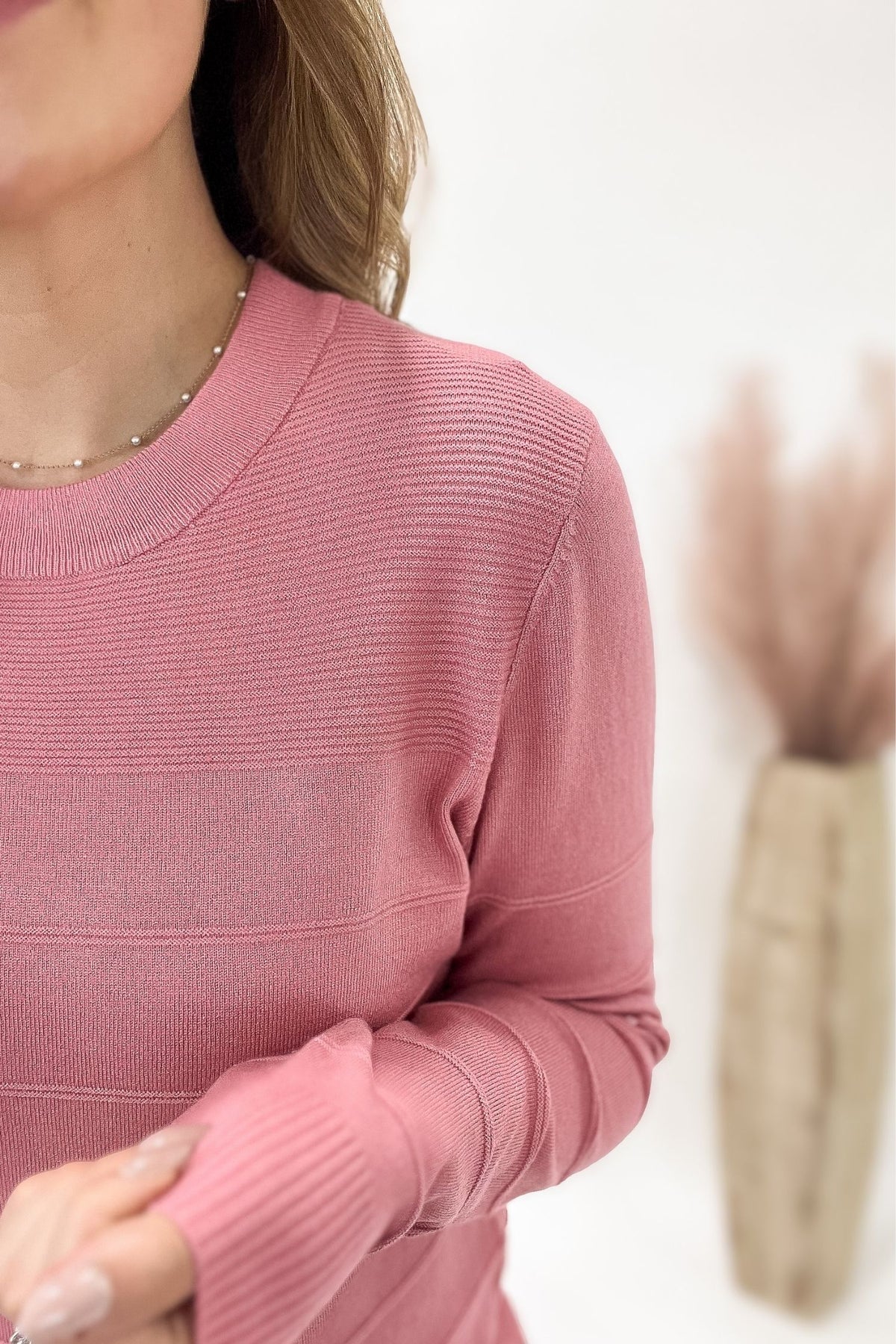 Close-up of a person wearing a pink ribbed sweater with a blurred background