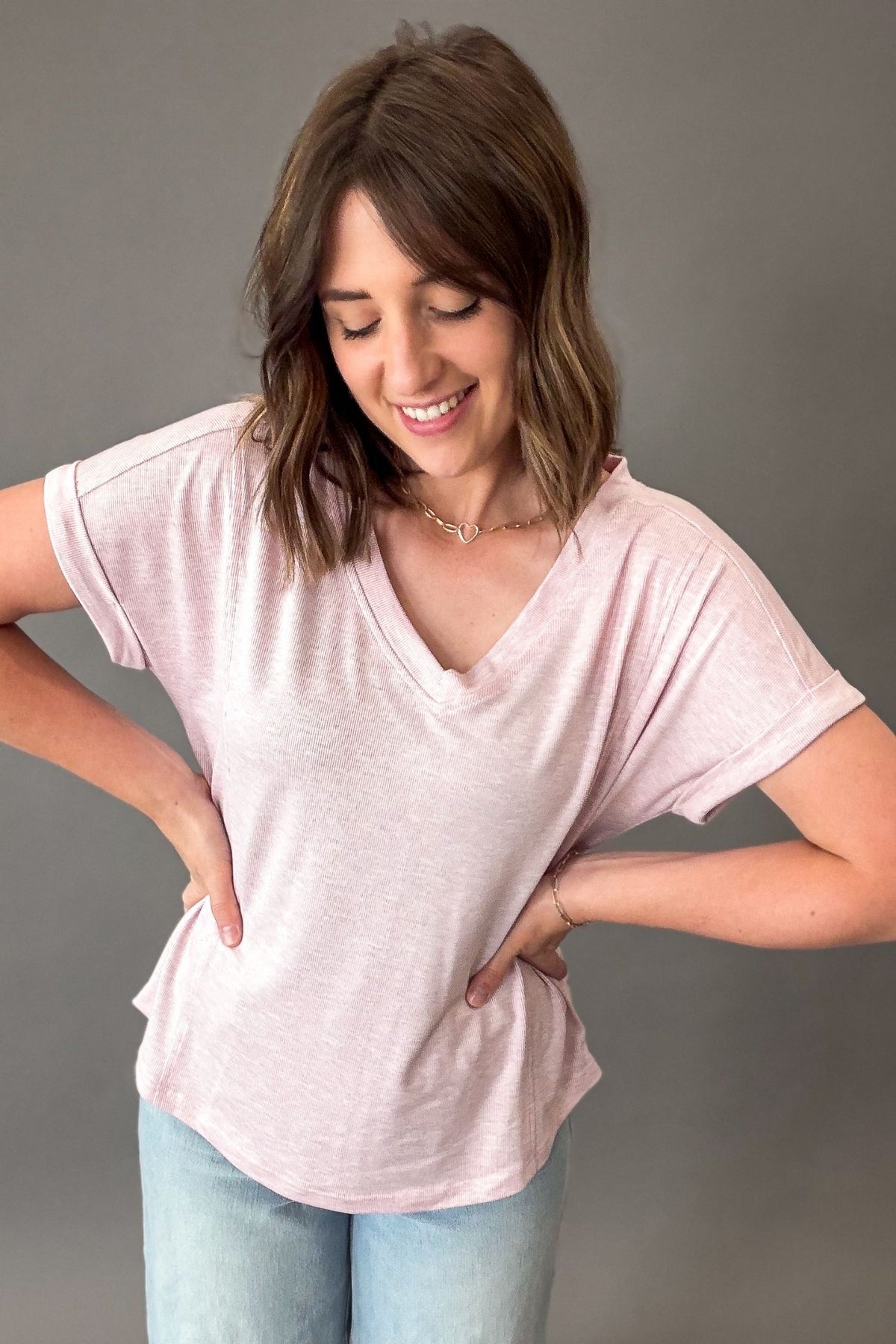 Woman wearing a light pink t-shirt and light blue jeans against a gray background
