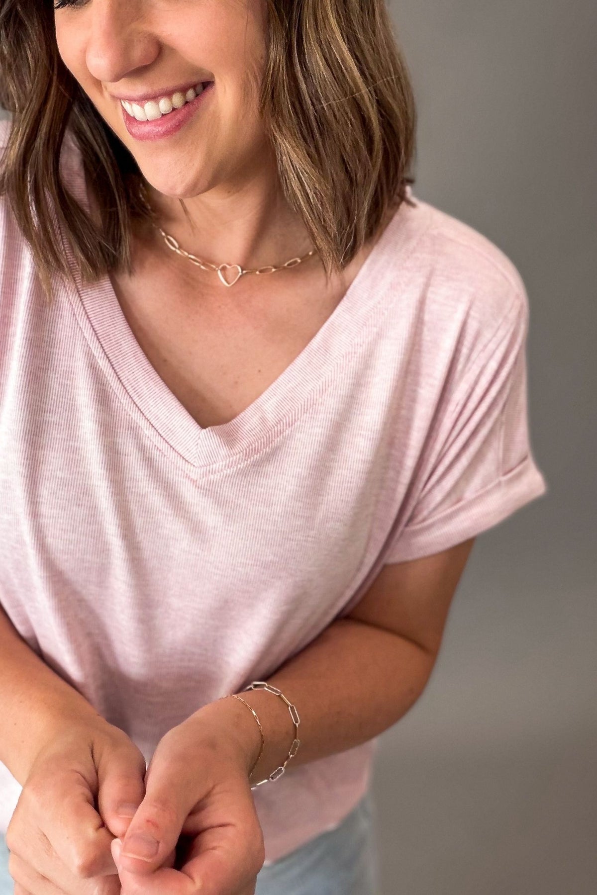 Woman wearing a pink shirt and gold jewelry on a gray background