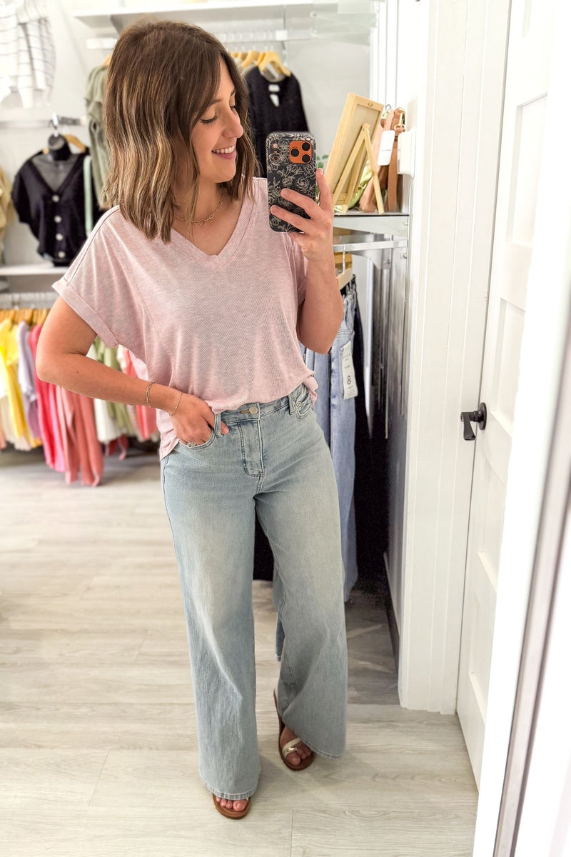 Woman taking a mirror selfie wearing a pink striped short sleeve and light blue jeans in a clothing store.