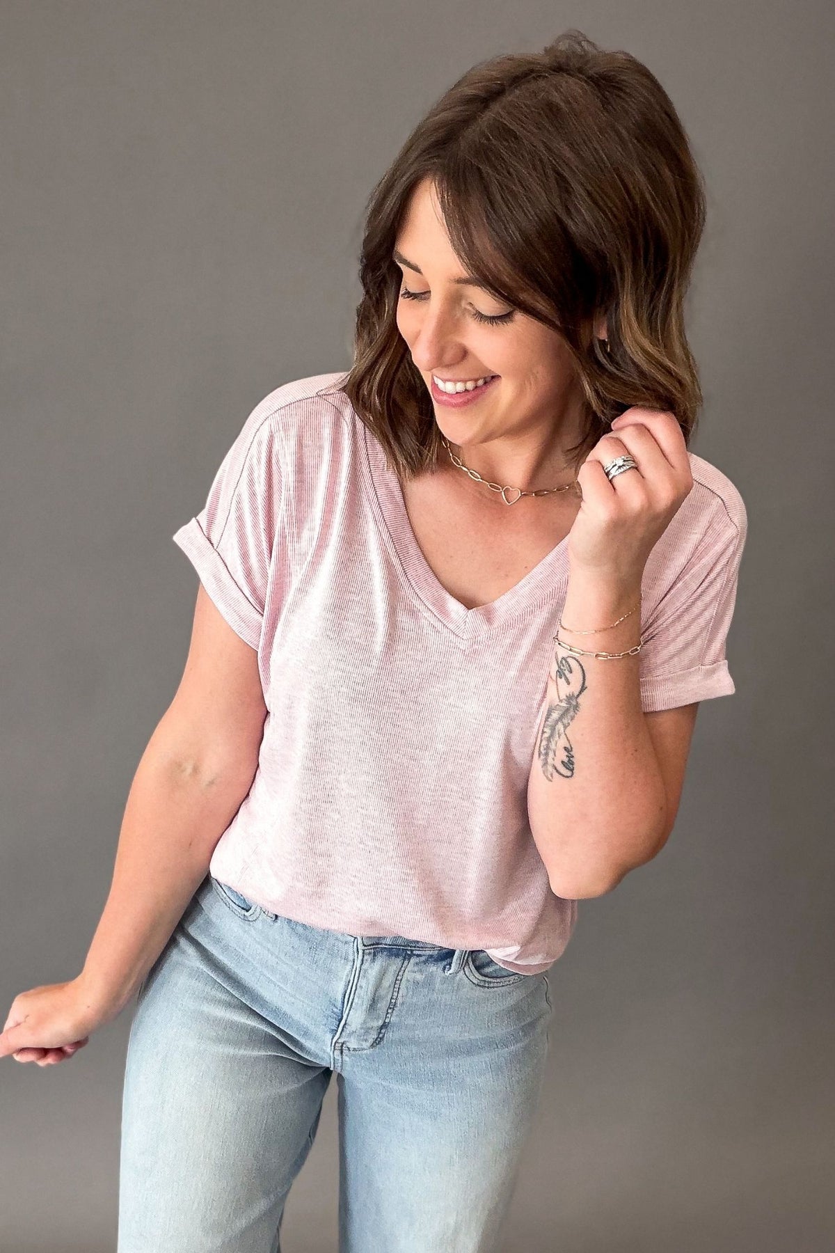 Woman wearing a light pink t-shirt and blue jeans against a gray background