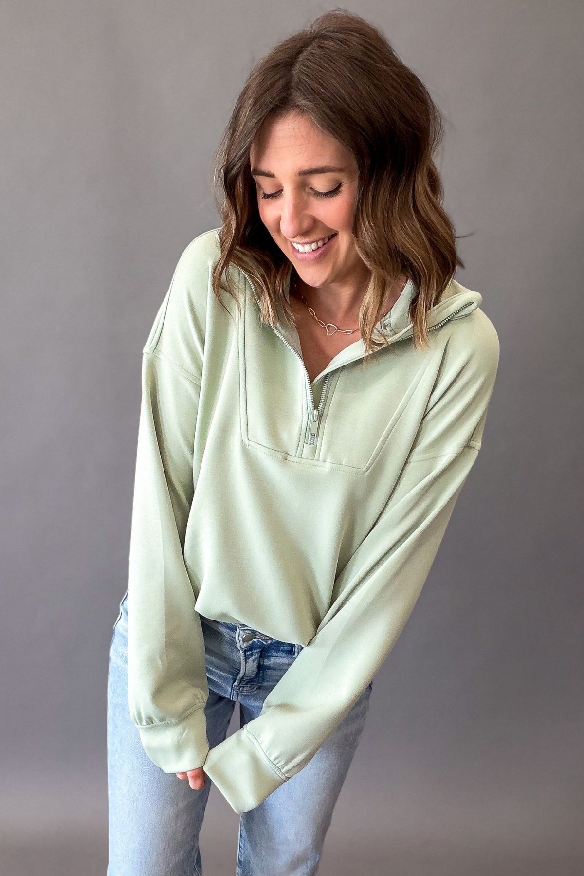 woman wearing a pistachio color quarter zip pullover and blue jeans on a grey background
