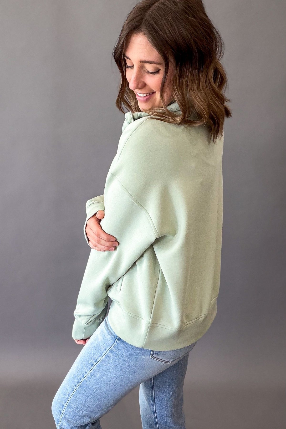woman wearing a pistachio quarter zip showing the side details and length
