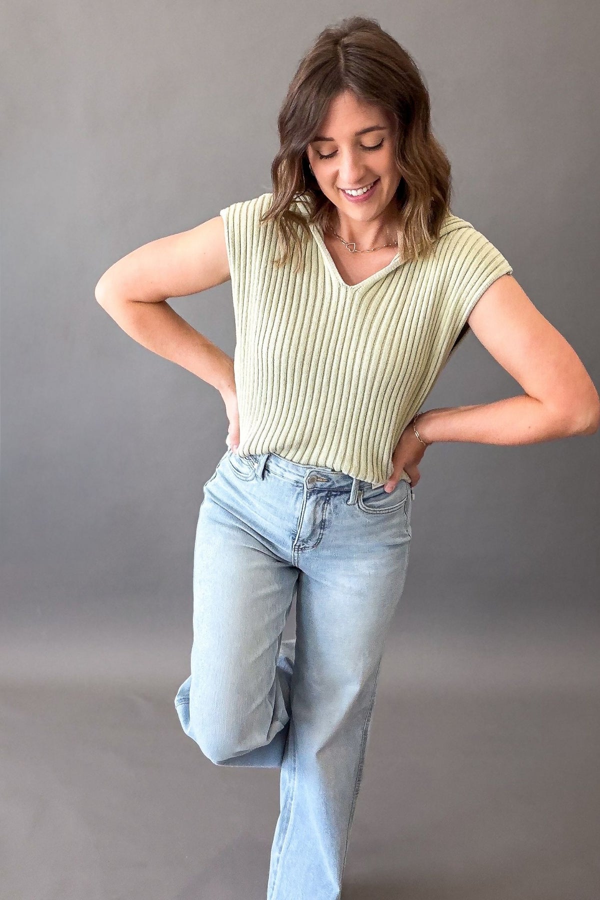 Woman wearing a green ribbed knit sweater tank with a light wash jean