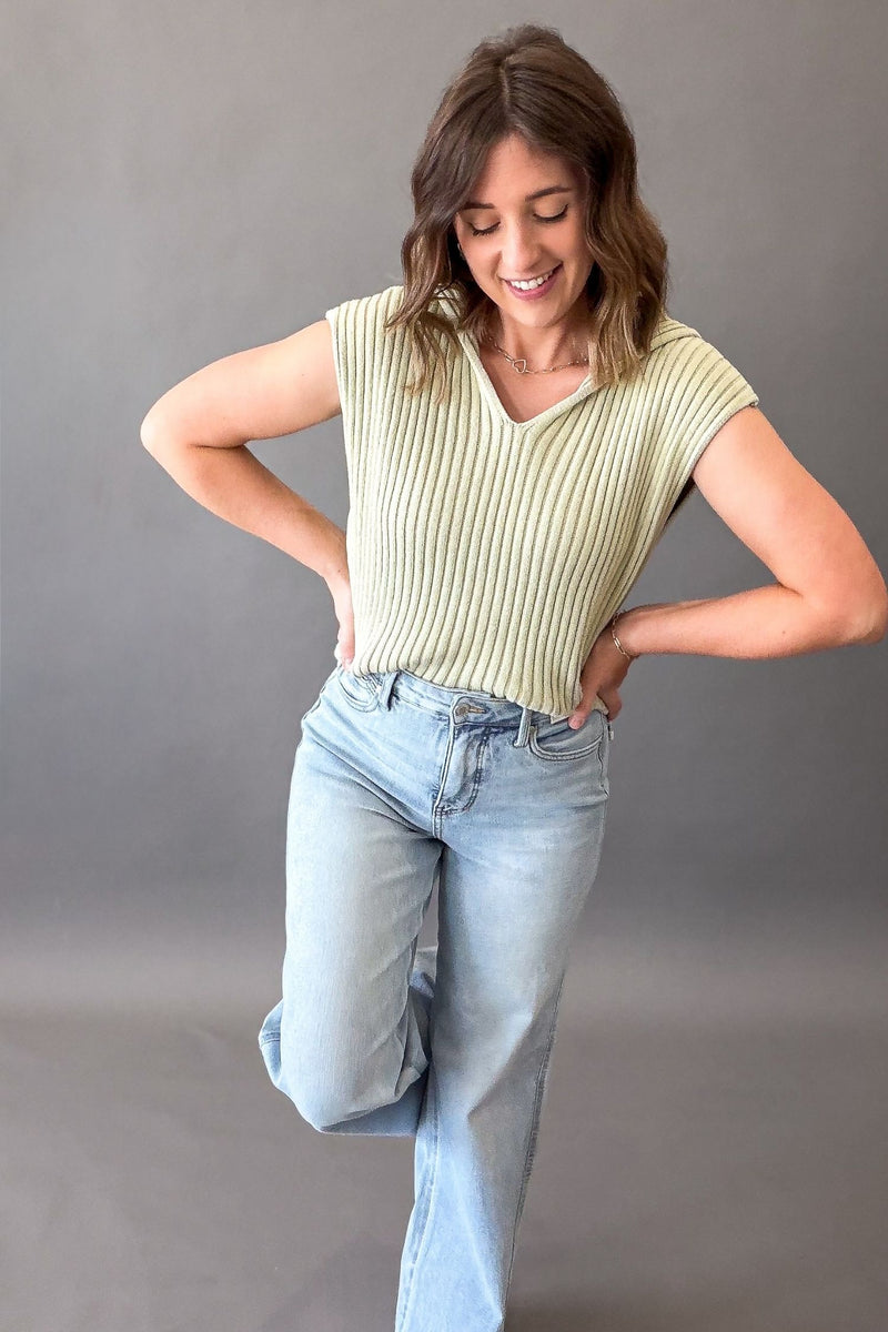 Woman wearing a green ribbed knit sweater tank with a light wash jean