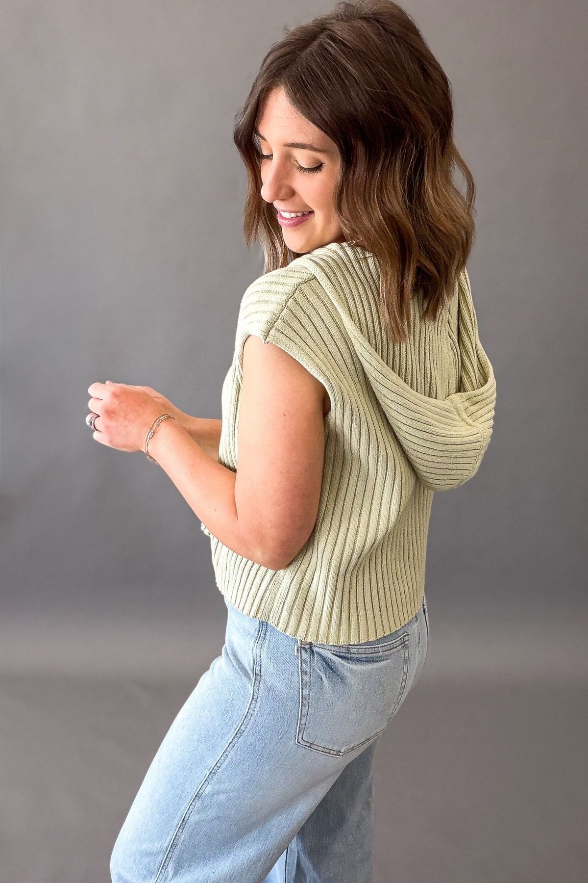 woman wearing a green ribbed top showing the side/back view with hoodie