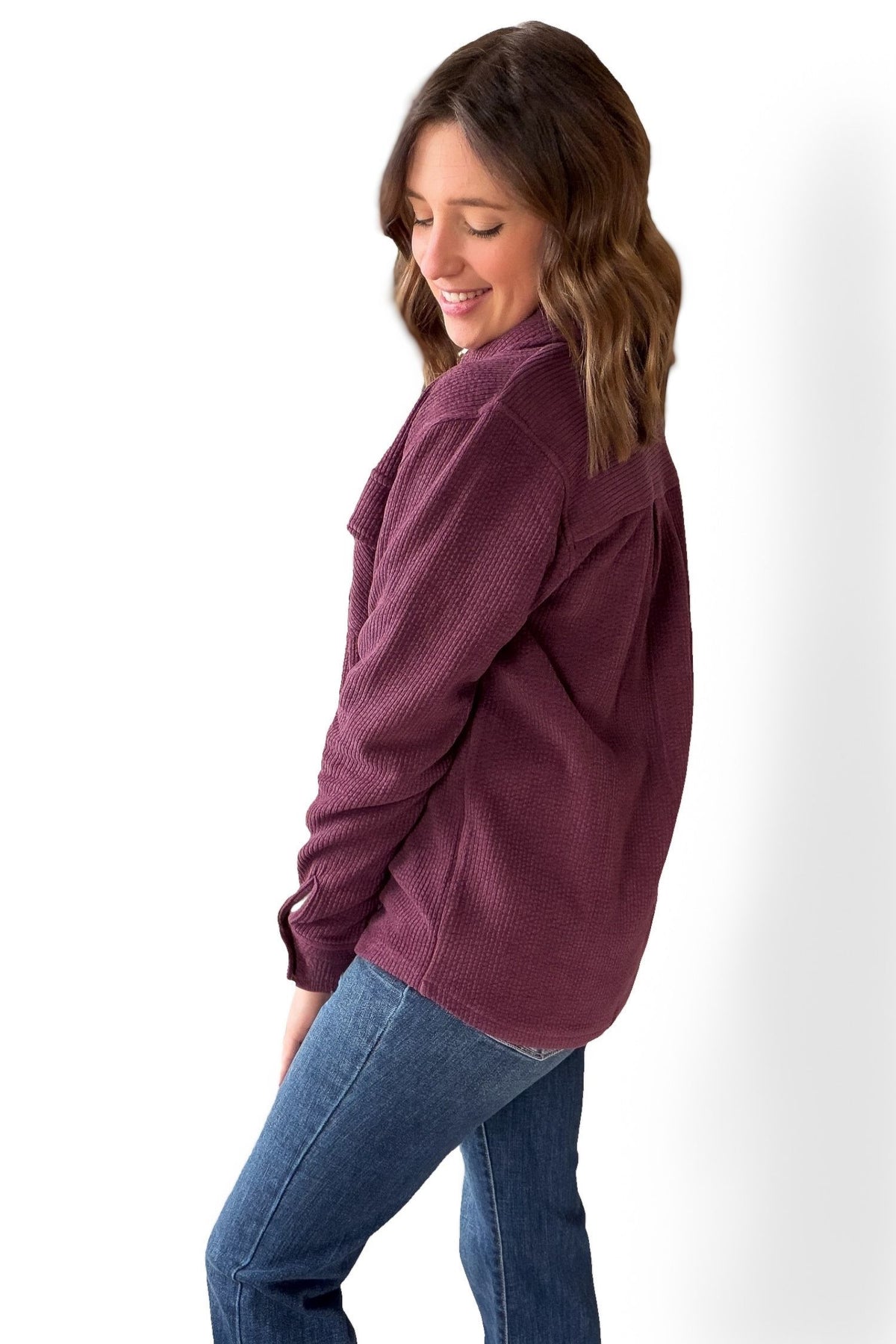Woman wearing a plum jacket and blue jeans on a white background