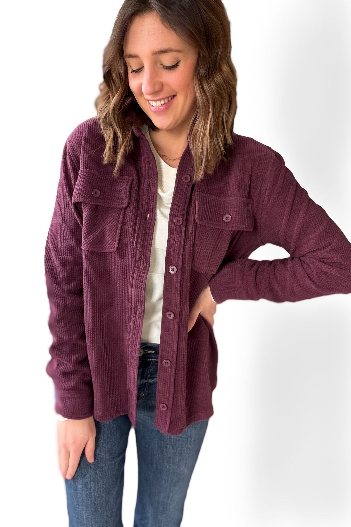 Woman wearing a plum jacket button up over a white top and blue jeans on a white background