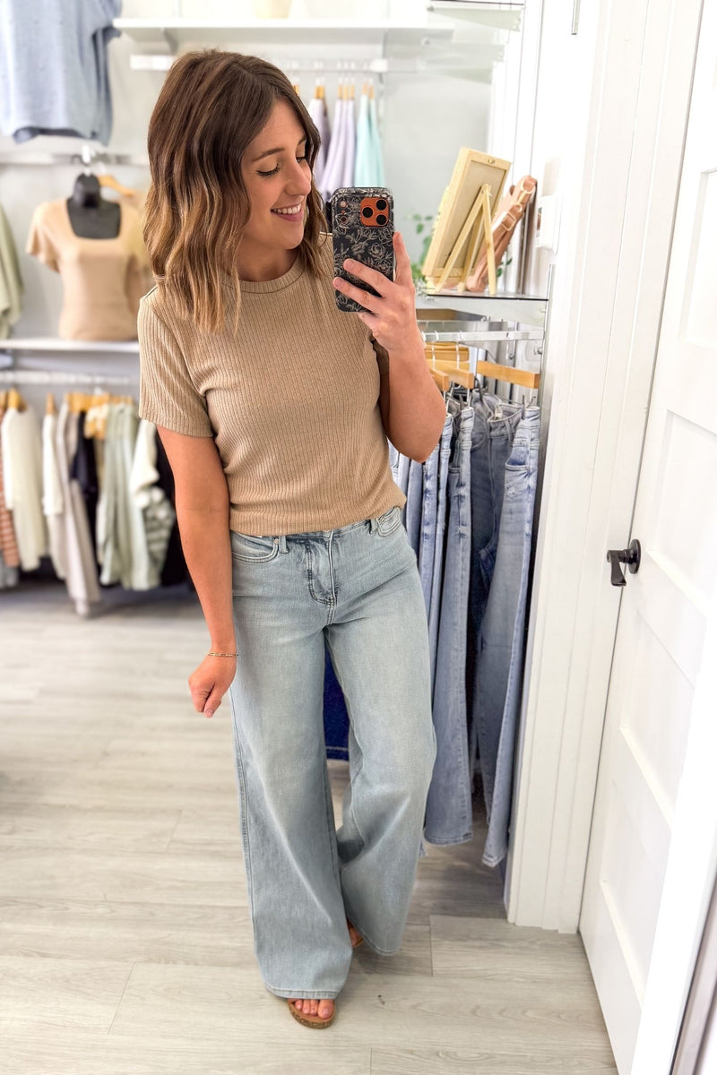 woman taking a selfie wearing a biscuit colored short sleeve with texture and light blue jeans in a womens boutique