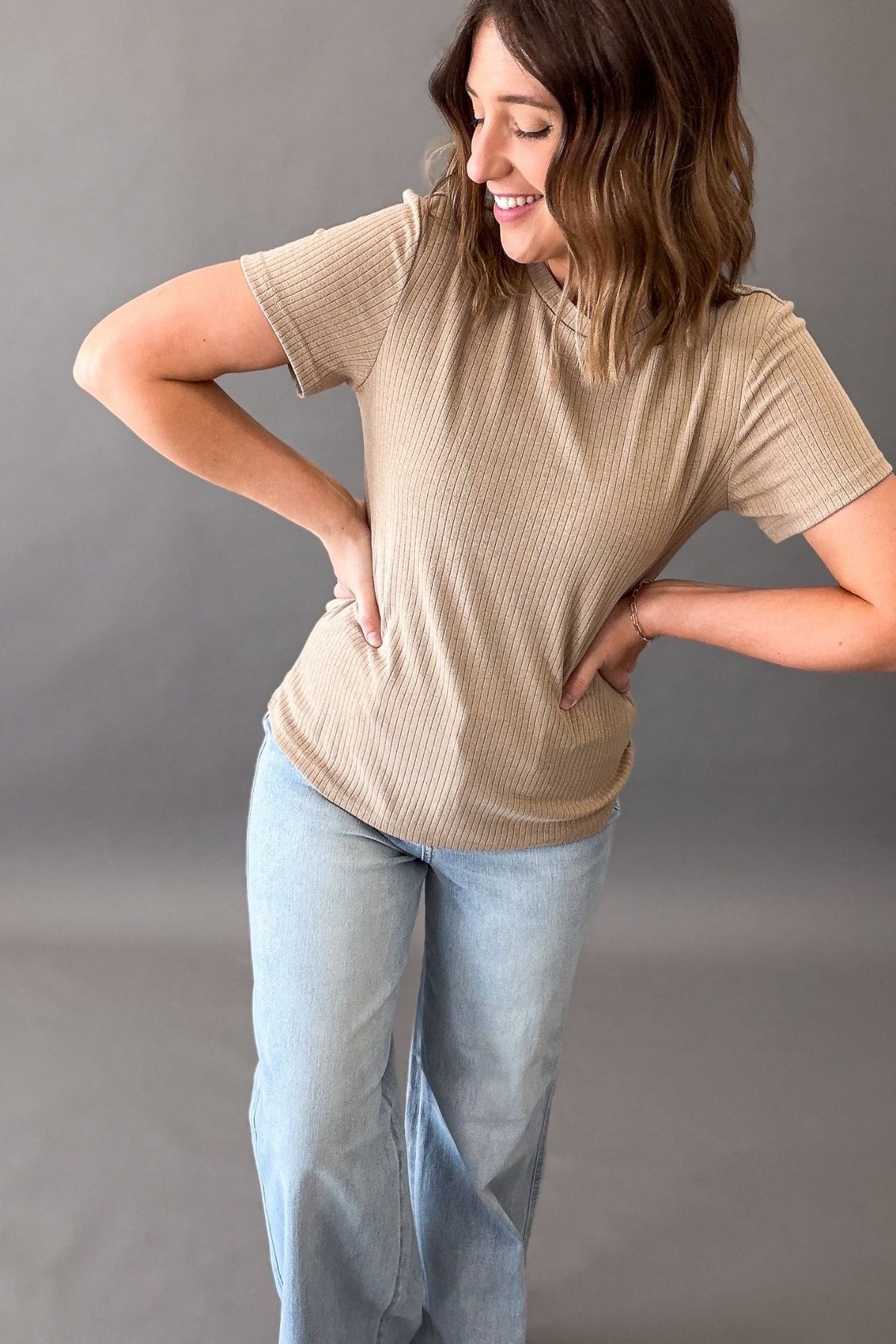 Woman wearing a elevated basic textured top with light blue jeans on a grey background