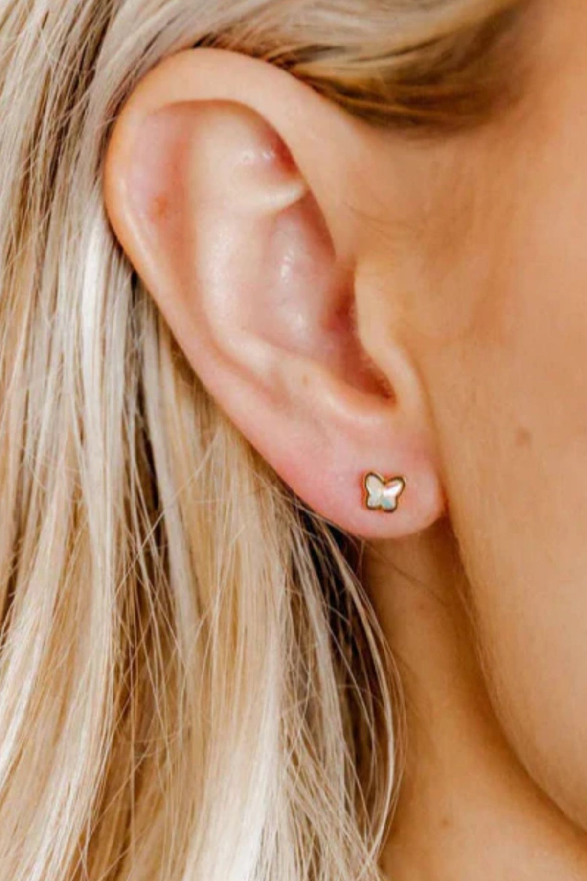 Close-up of an ear wearing a gold butterfly earring with blonde hair.
