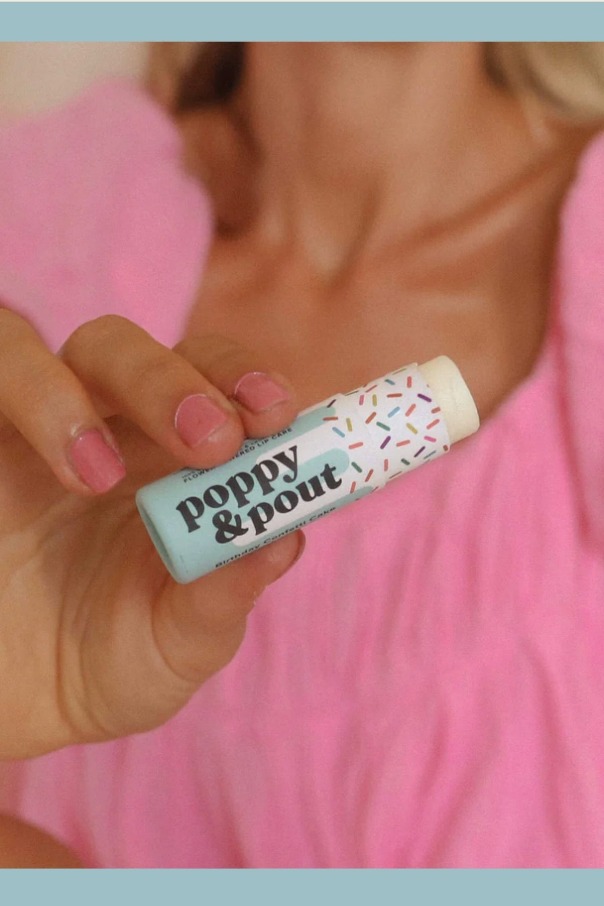 Hand holding a lip balm with 'Poppy & Pout' branding against a pink background