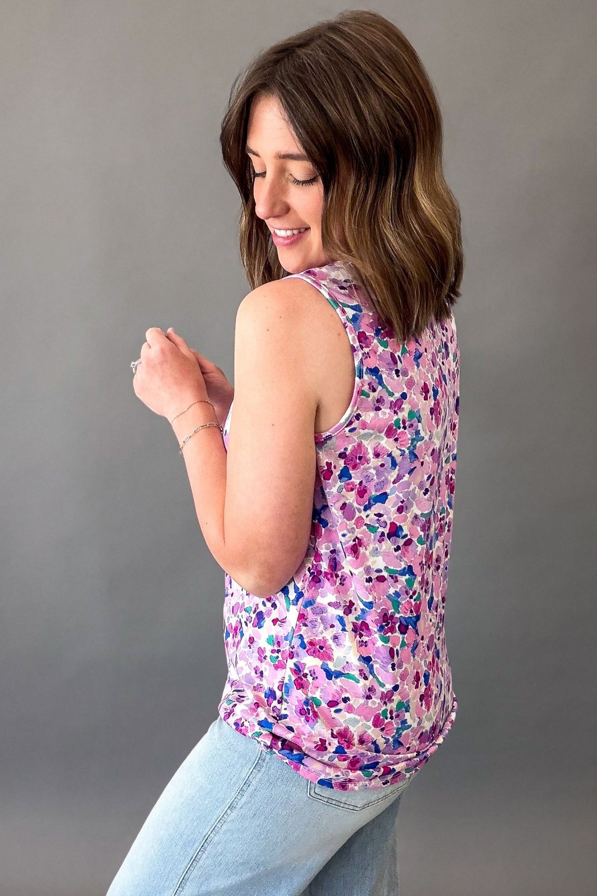 Woman wearing a purple floral sleeveless tank top featuring a colorful watercolor floral print and relaxed fit showing side and back details