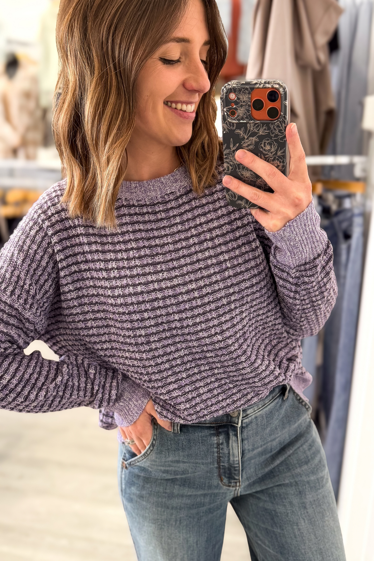 A woman takes a mirror selfie wearing a textured, ribbed knit sweater in a dusty lavender-purple color, paired with blue jeans.