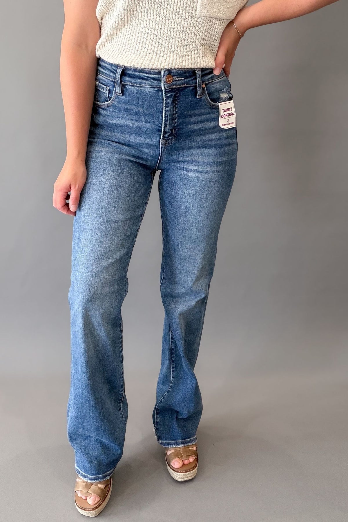 Woman wearing RISEN high-rise tummy control straight leg jeans in a rich dark wash with subtle distressing near the pocket and hem.