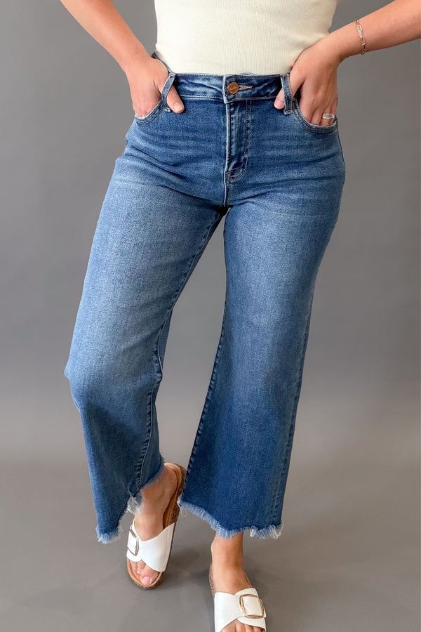 Woman wearing RISEN mid rise crop straight jeans with a medium wash, raw hem, and flattering straight-leg fit.