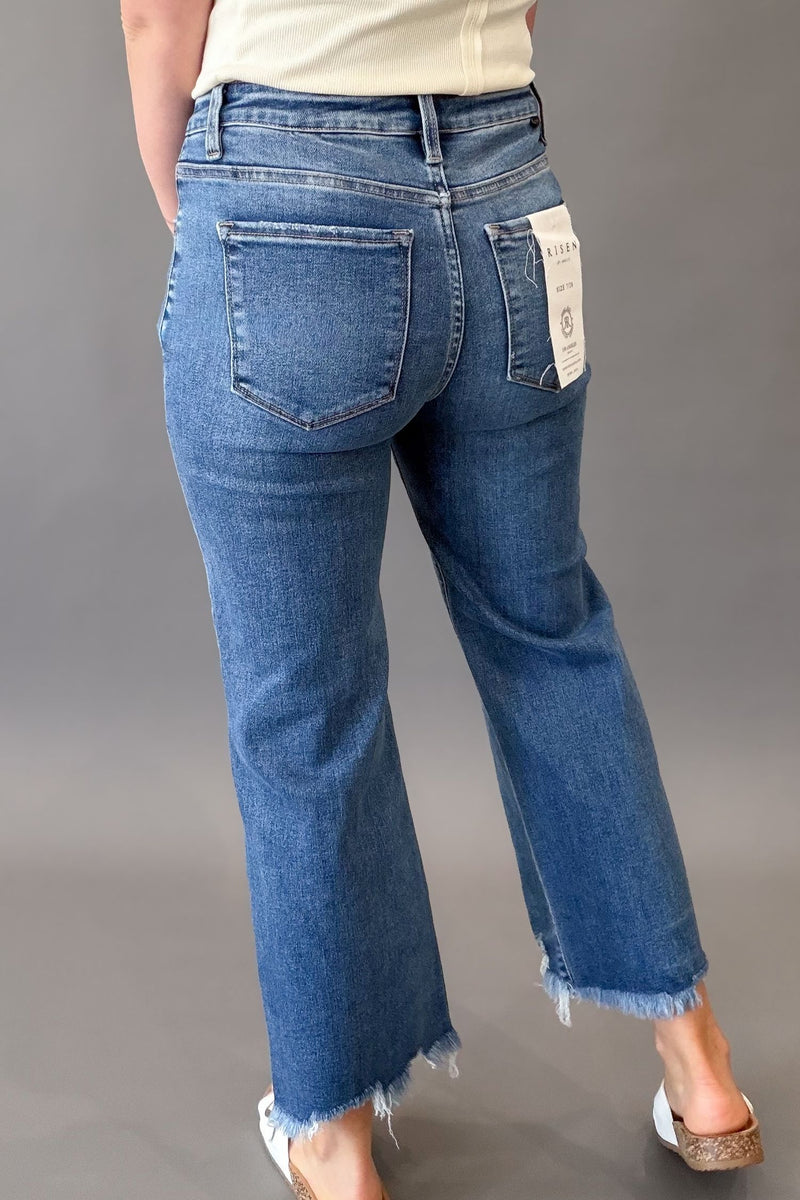 Woman wearing RISEN mid rise crop straight jeans with a medium wash, raw hem, and flattering straight-leg fit showing back details
