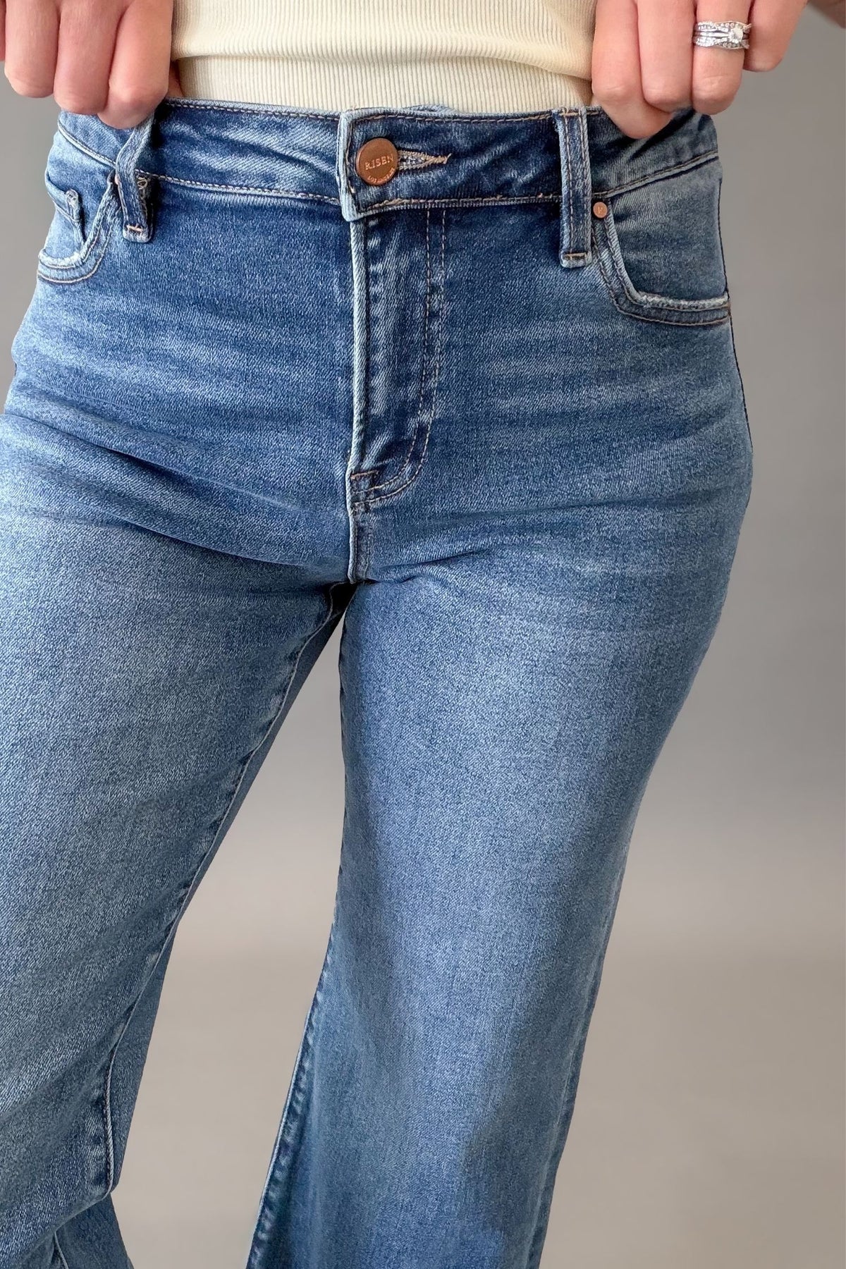 Woman wearing RISEN mid rise crop straight jeans with a medium wash, raw hem, and flattering straight-leg fit showing close up denim details