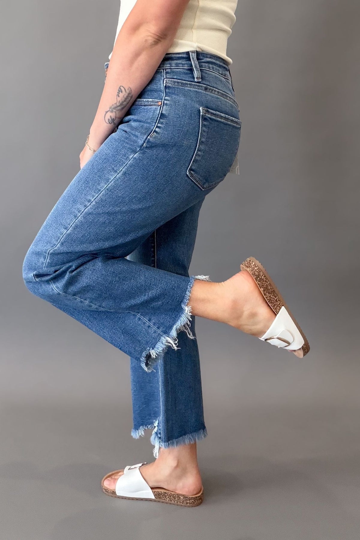 Woman wearing RISEN mid rise crop straight jeans with a medium wash, raw hem, and flattering straight-leg fit showing side details