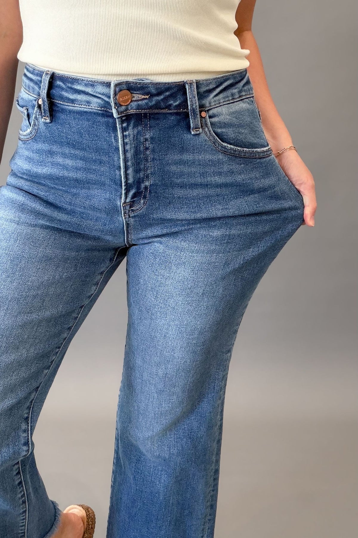 Woman wearing RISEN mid rise crop straight jeans with a medium wash, raw hem, and flattering straight-leg fit showing stretch in the denim.