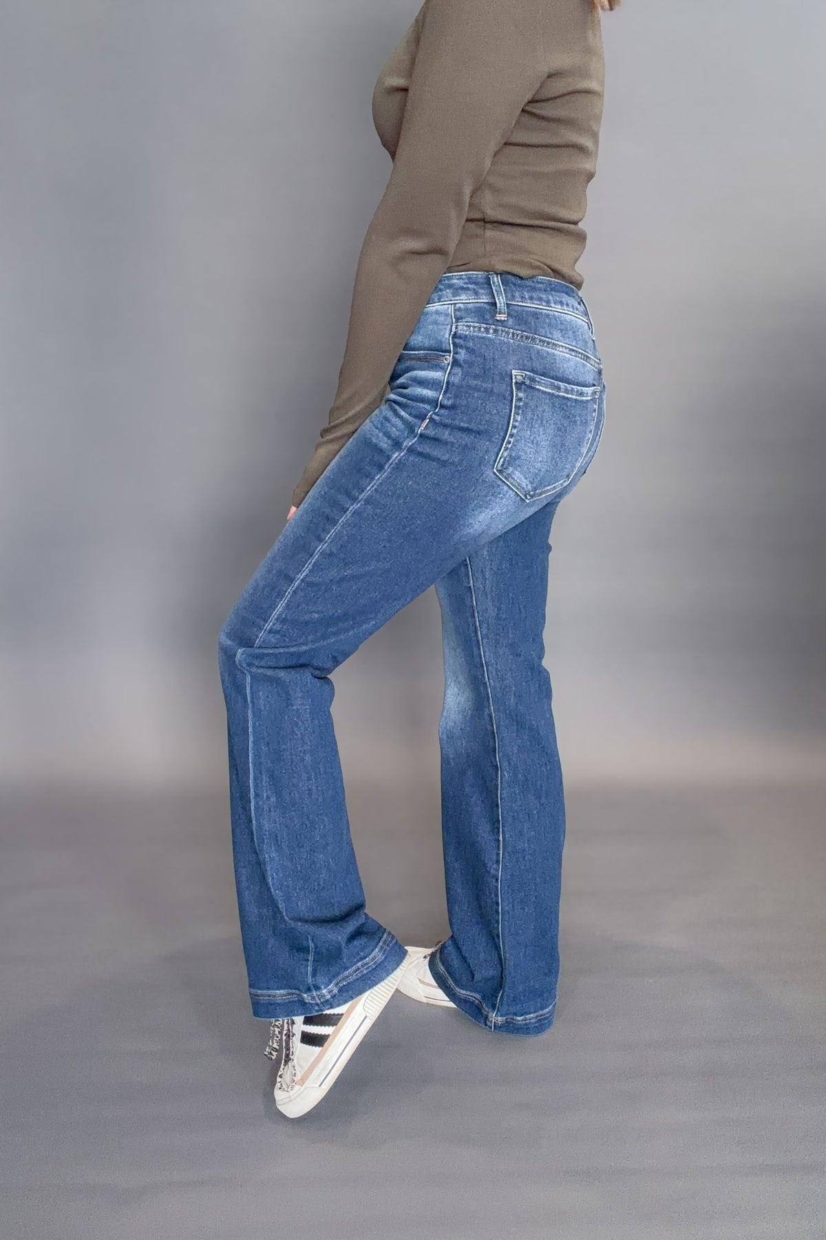 Person wearing blue jeans and a green top on a gray background showing the side view of the denim