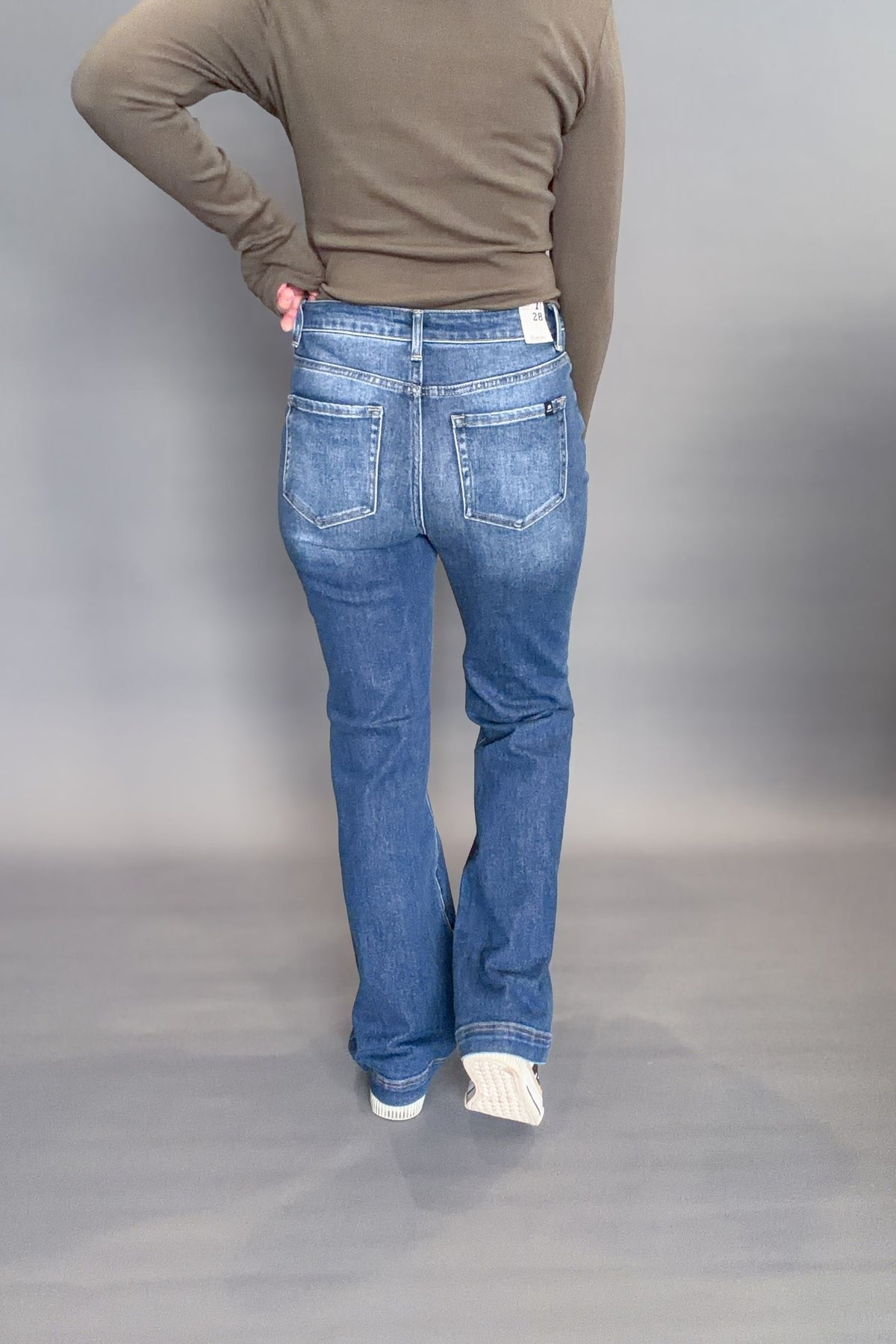 Person wearing blue jeans and a green top on a plain background showing the back of the denim.
