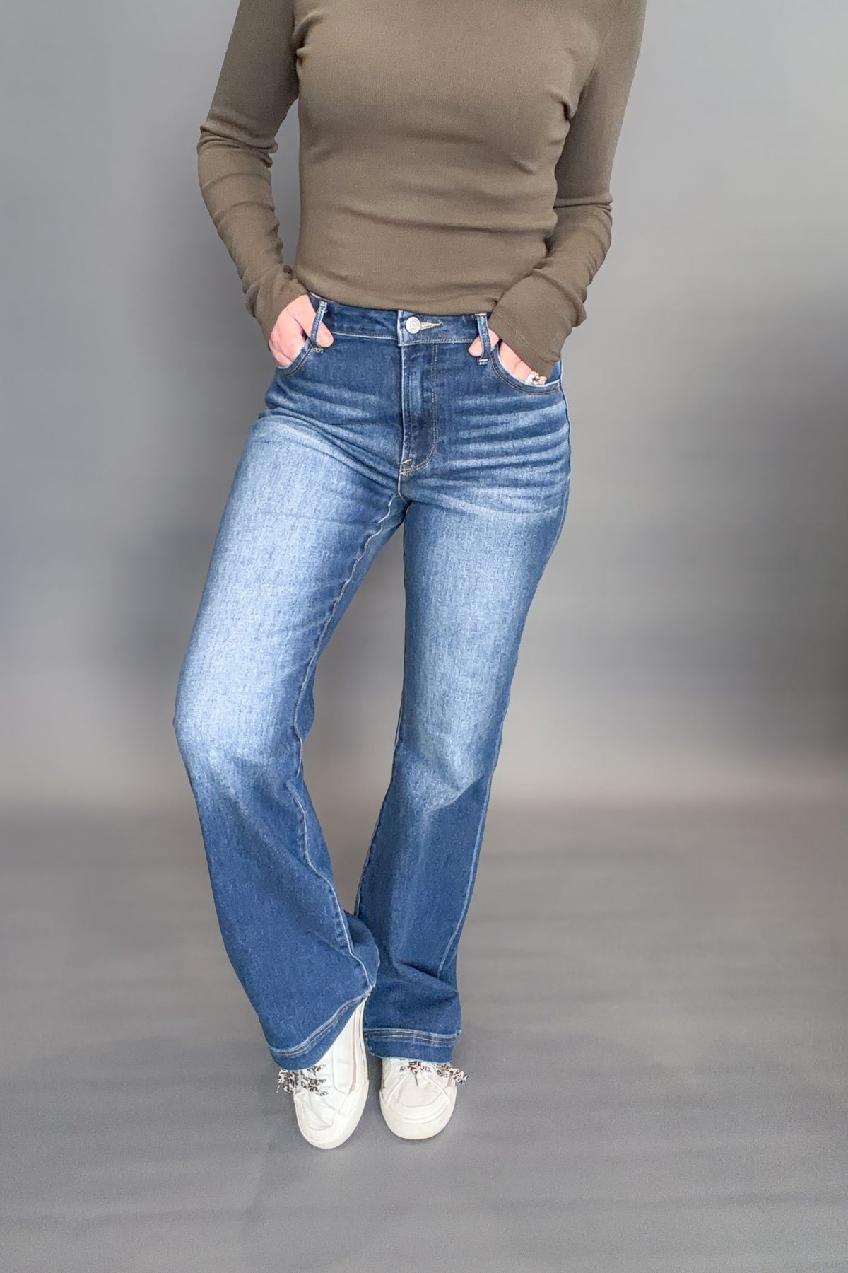 Person wearing blue jeans and a green long-sleeve shirt on a gray background