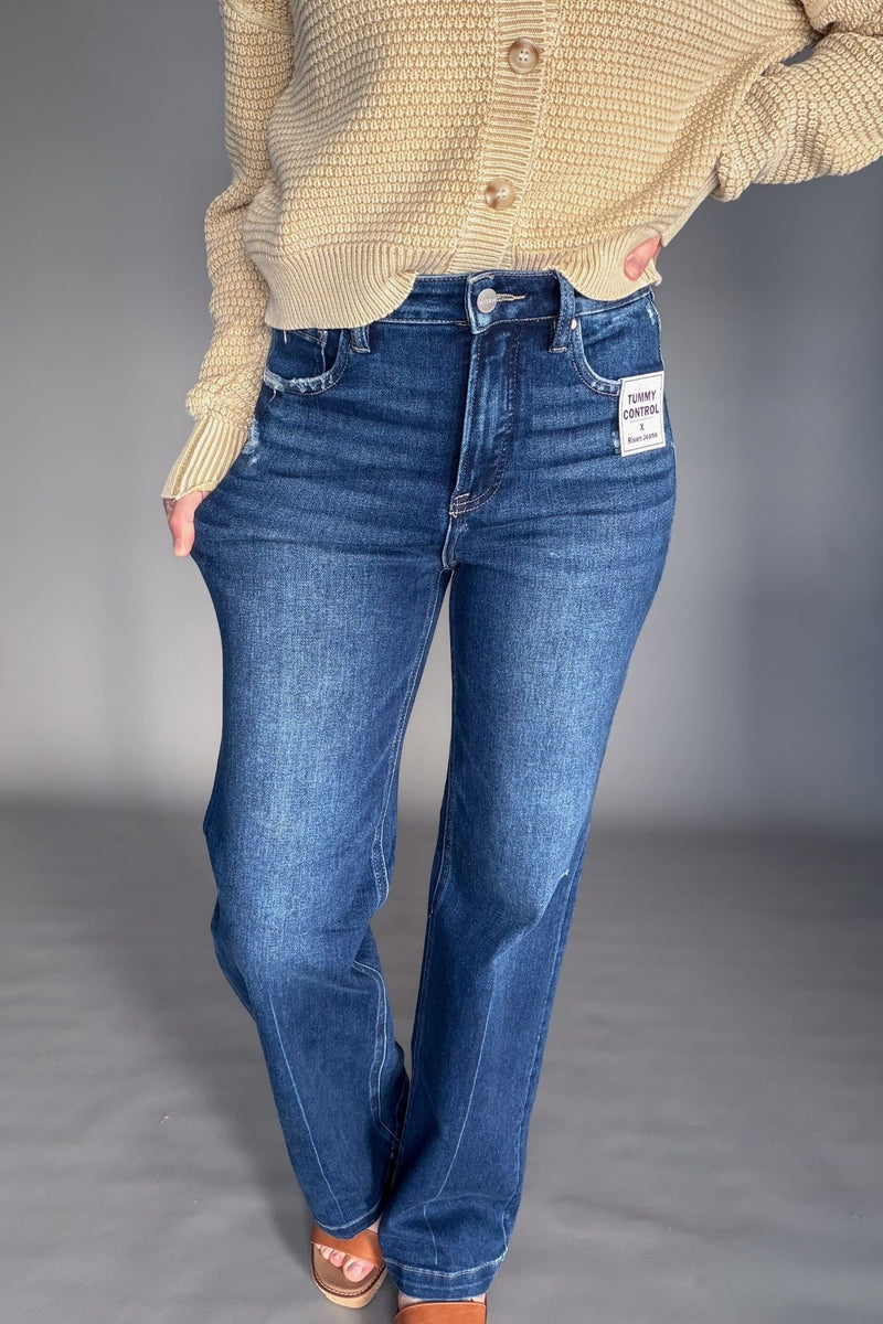 Person wearing blue jeans and a beige cardigan on a plain background