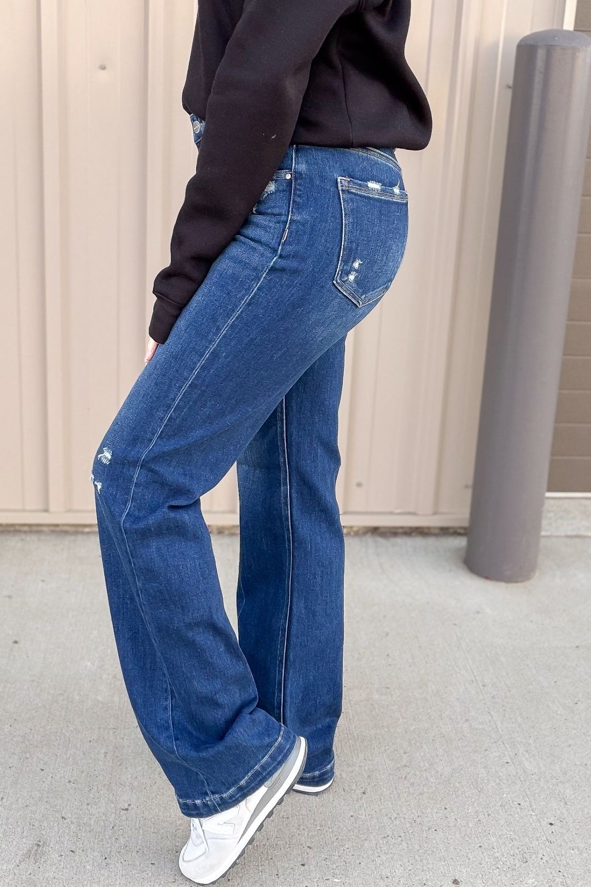 Person wearing blue jeans and a black top against a plain background