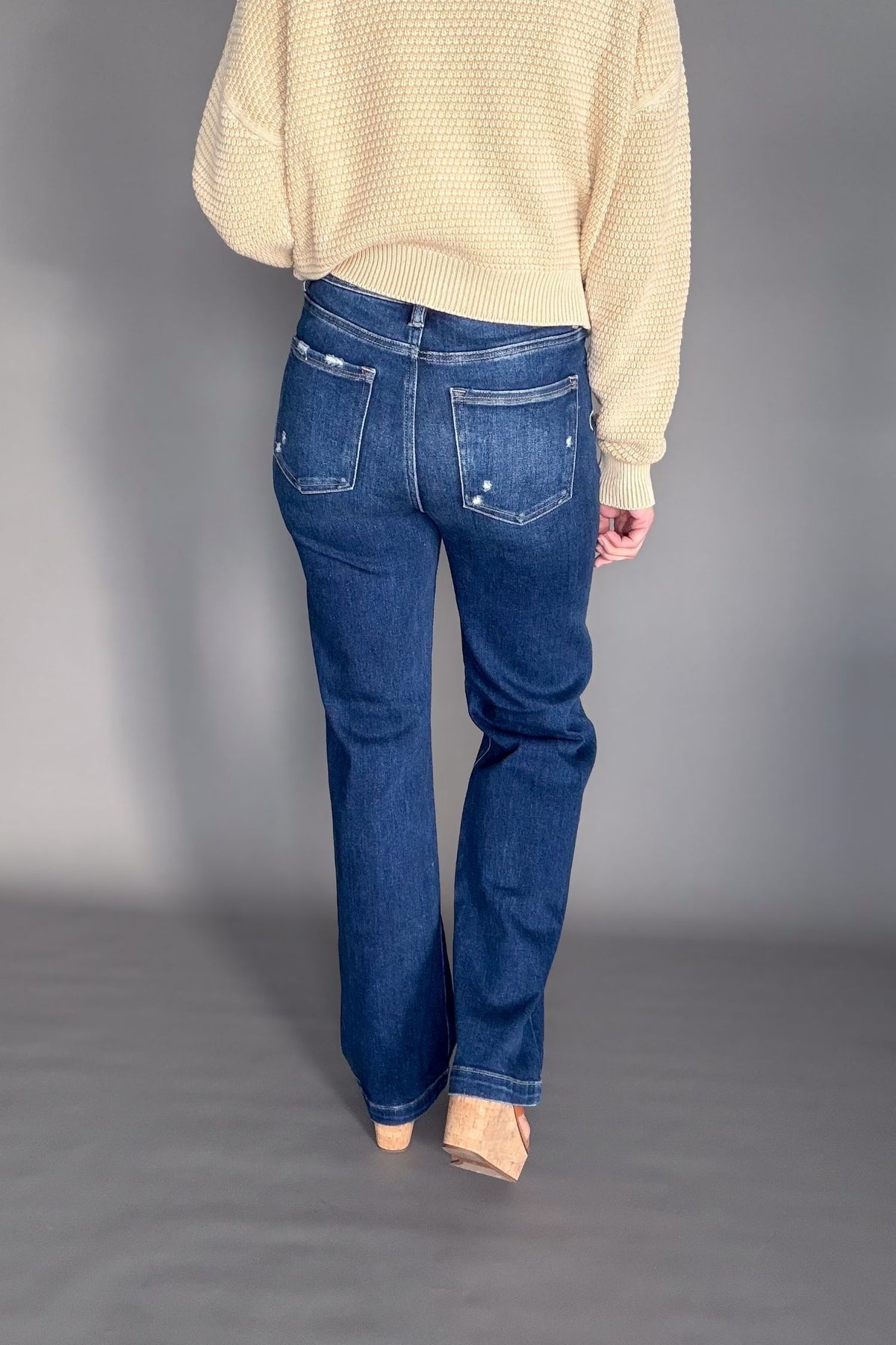 Person wearing blue jeans and a camel sweater on a plain background