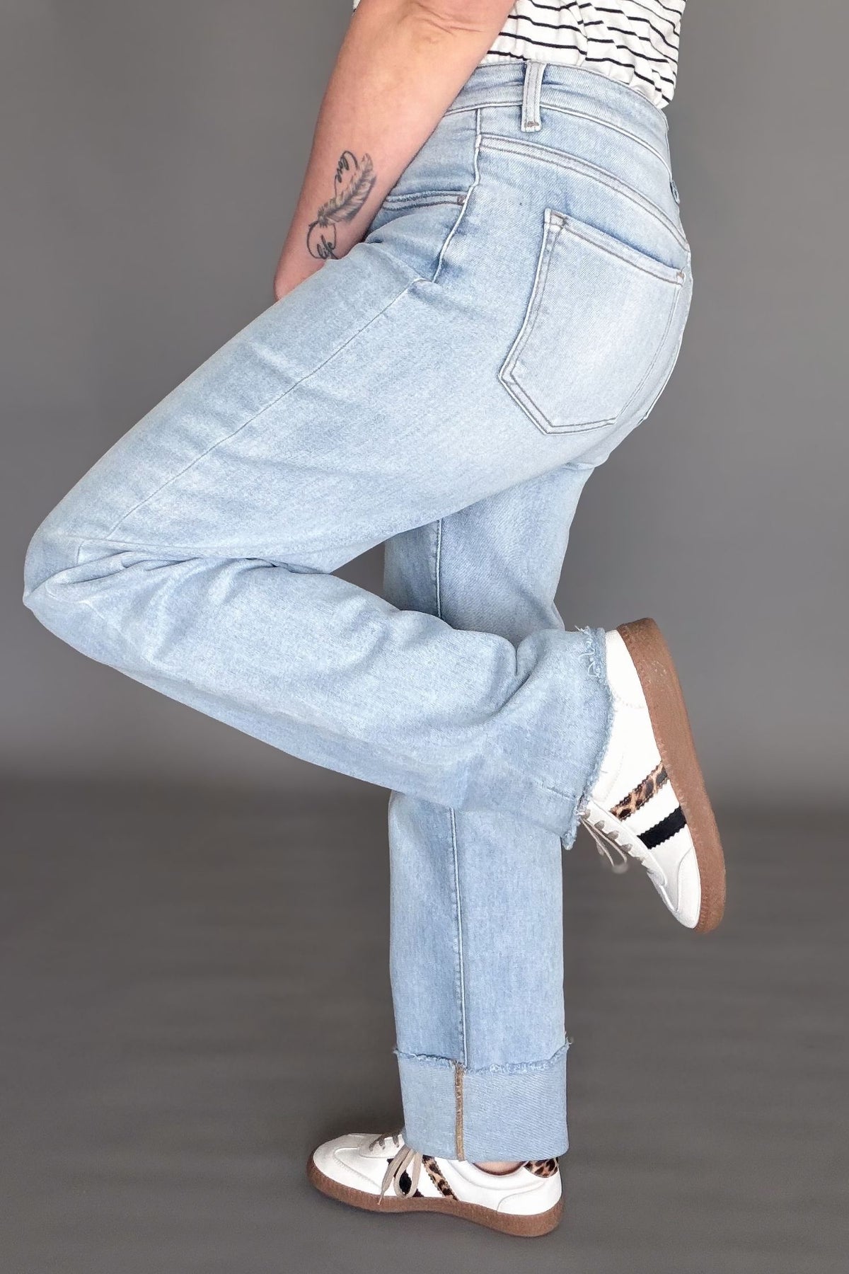 Woman wearing a light wash risen high rise straight cuffed denim on a dark grey background showing the side view and both cuffed and uncuffed 
