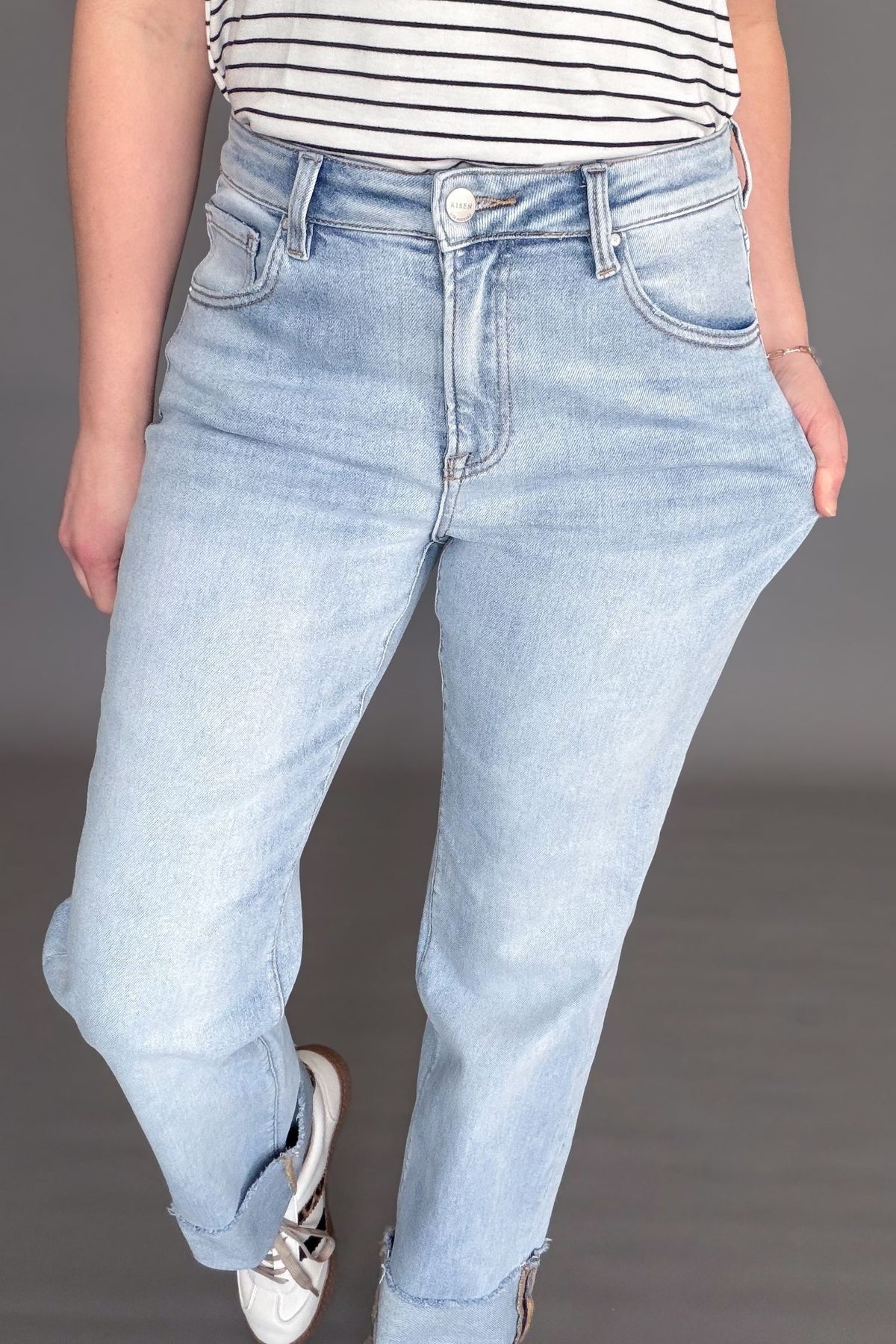 Woman wearing a light wash risen high rise straight cuffed denim on a dark grey background showing the stretch