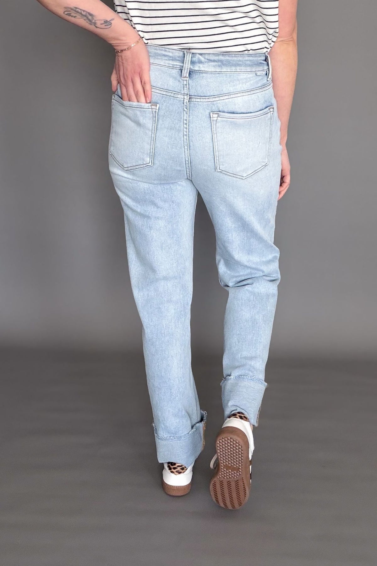 Woman wearing a light wash risen high rise straight cuffed denim on a dark grey background showing the back of the denim