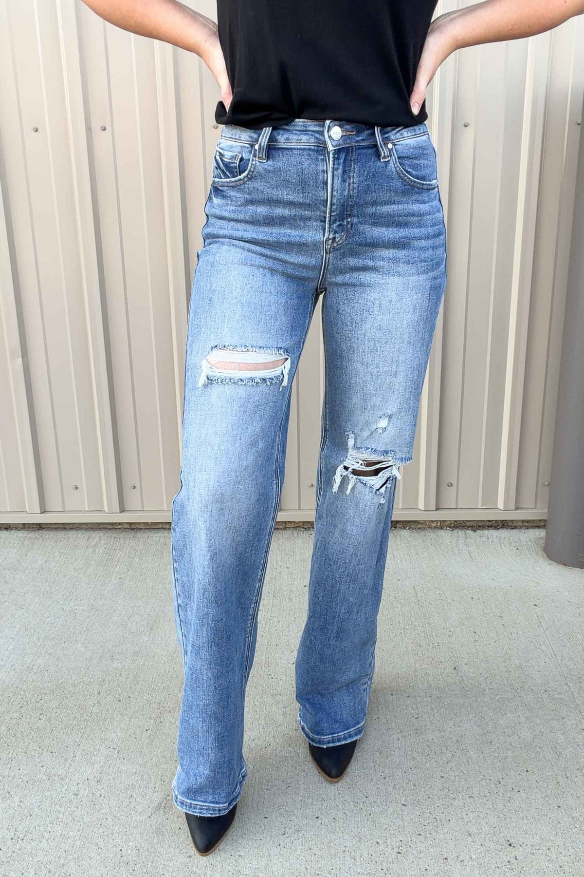 Person wearing blue jeans with distressed details against a neutral background