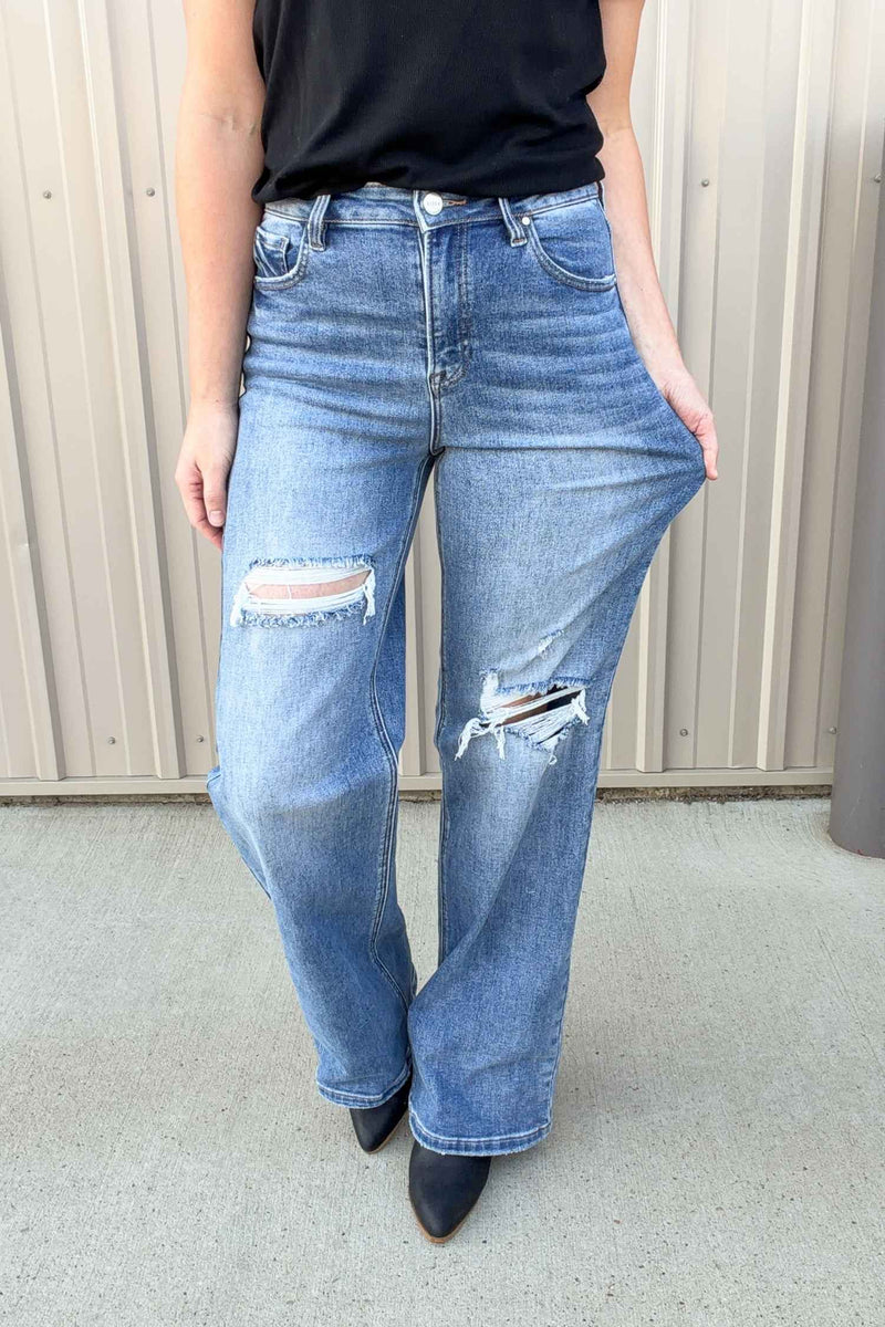 Person wearing blue distressed jeans against a neutral background
