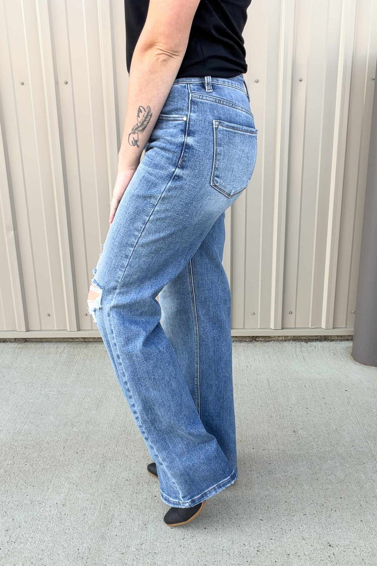 Person wearing blue jeans standing against a beige wall.
