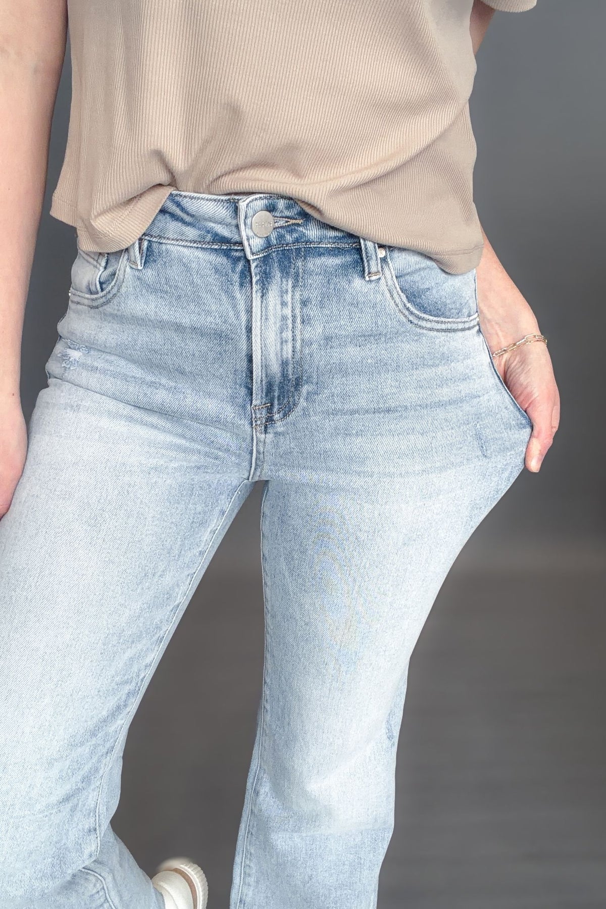 Woman wearing Risen Kathleen High Rise Ankle Flare Jeans on a grey background with white sneakers and a taupe tee 