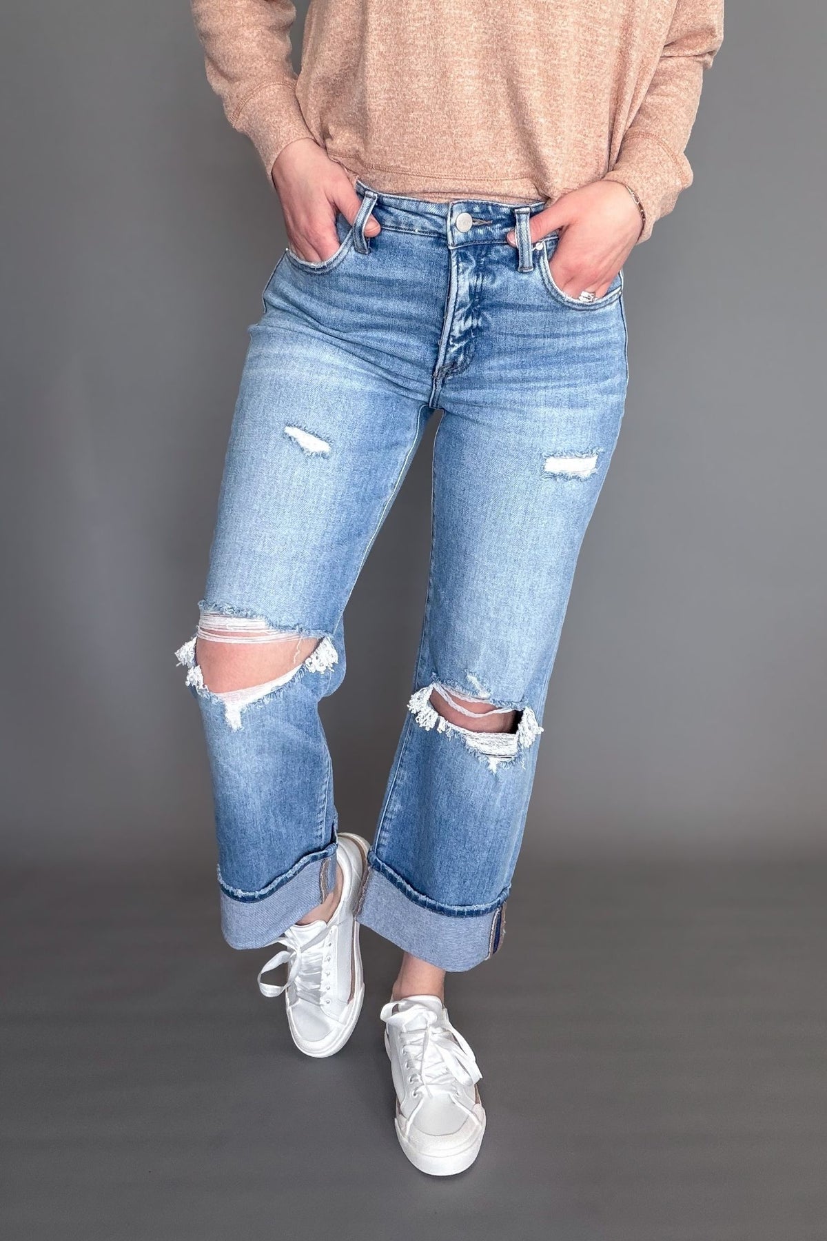 Person wearing distressed blue jeans and white sneakers on a gray background