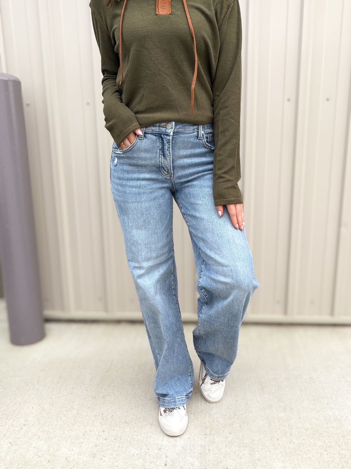 Person wearing a olive hoodie and blue jeans standing against a neutral background