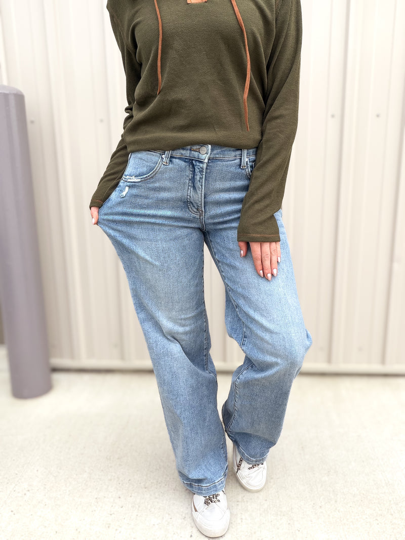 Person wearing a green long-sleeve shirt and blue jeans against a neutral background