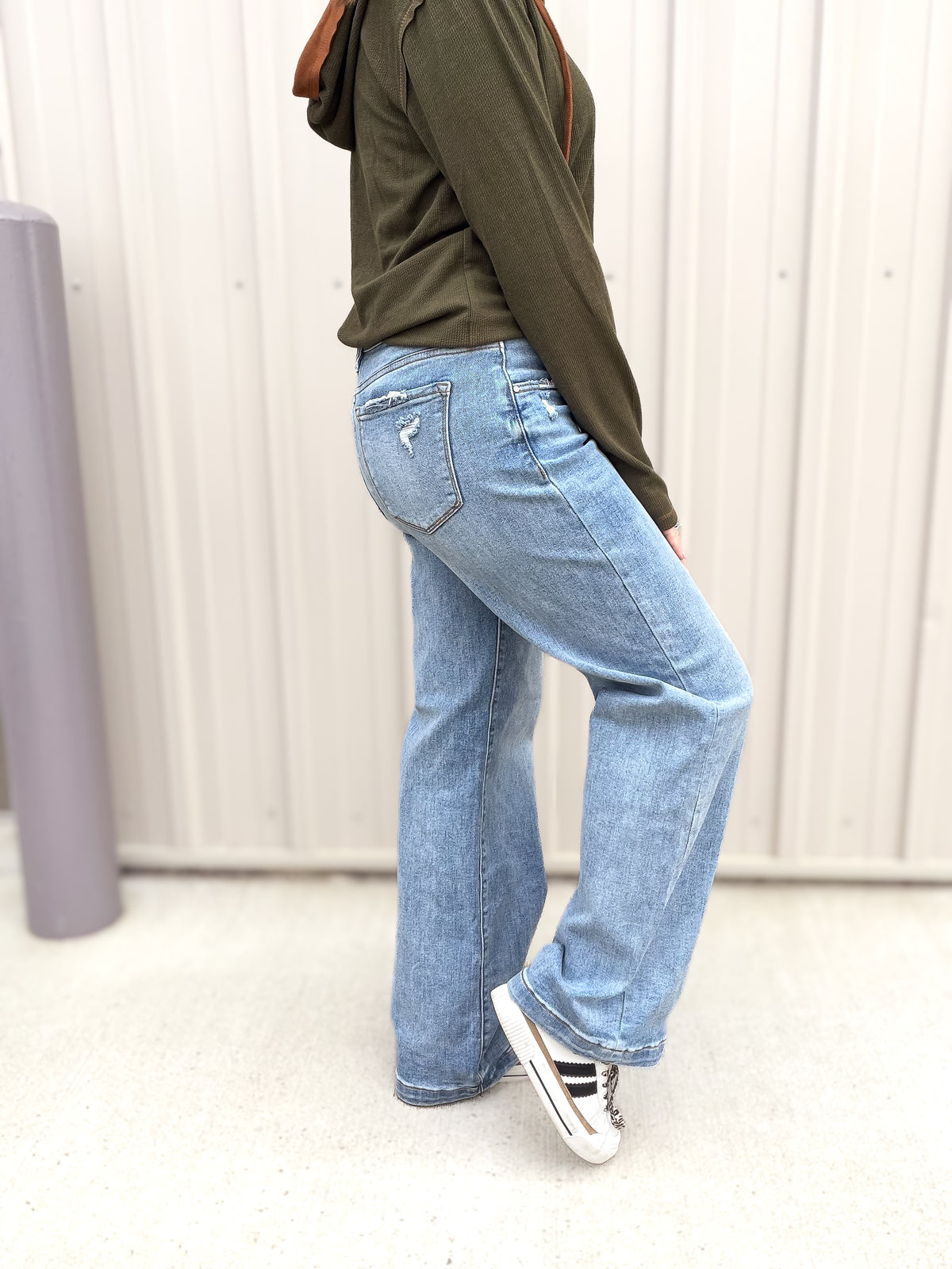 Person wearing blue jeans and a green hoodie in a minimal indoor setting