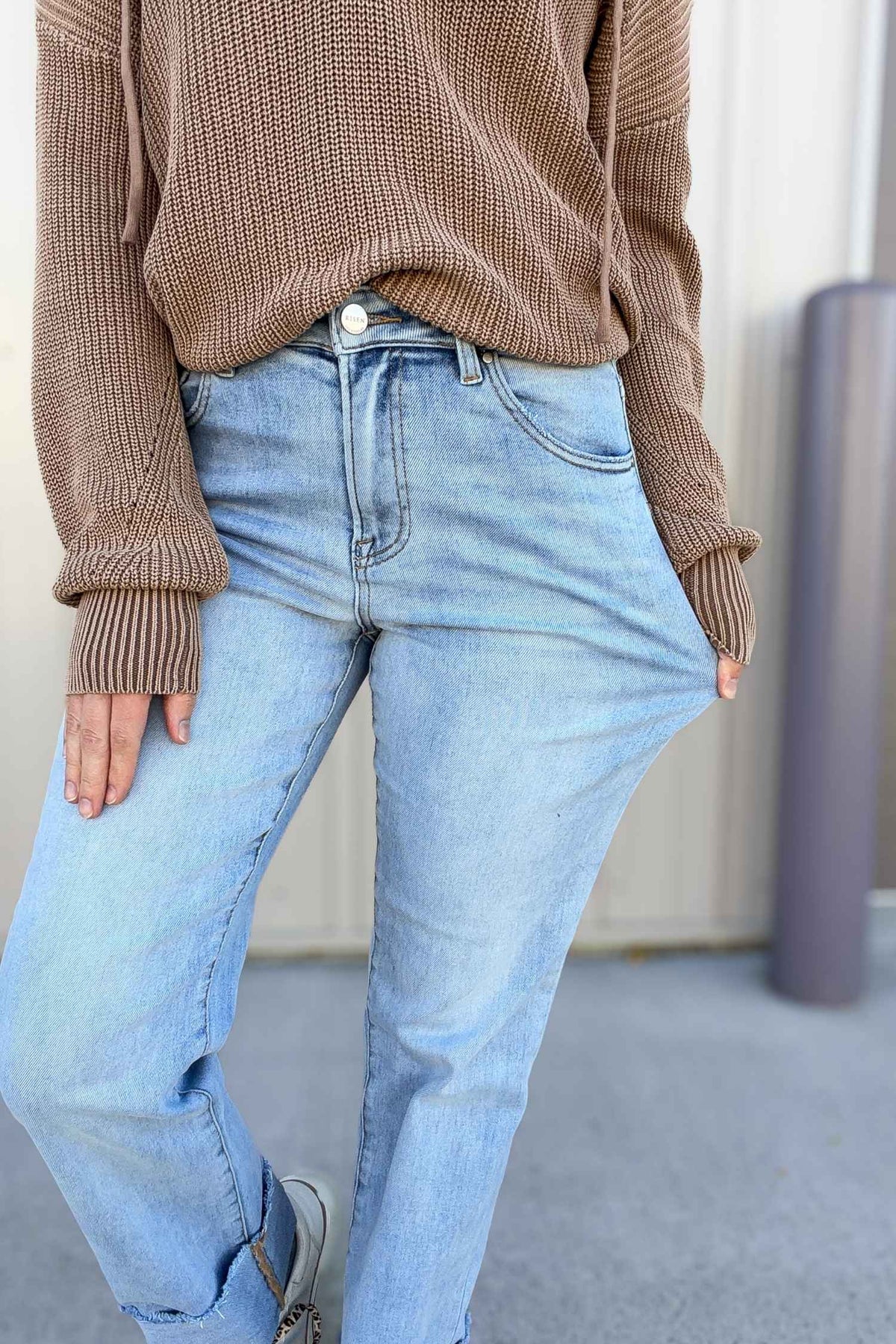 Person wearing a brown sweater and light blue jeans against a neutral background