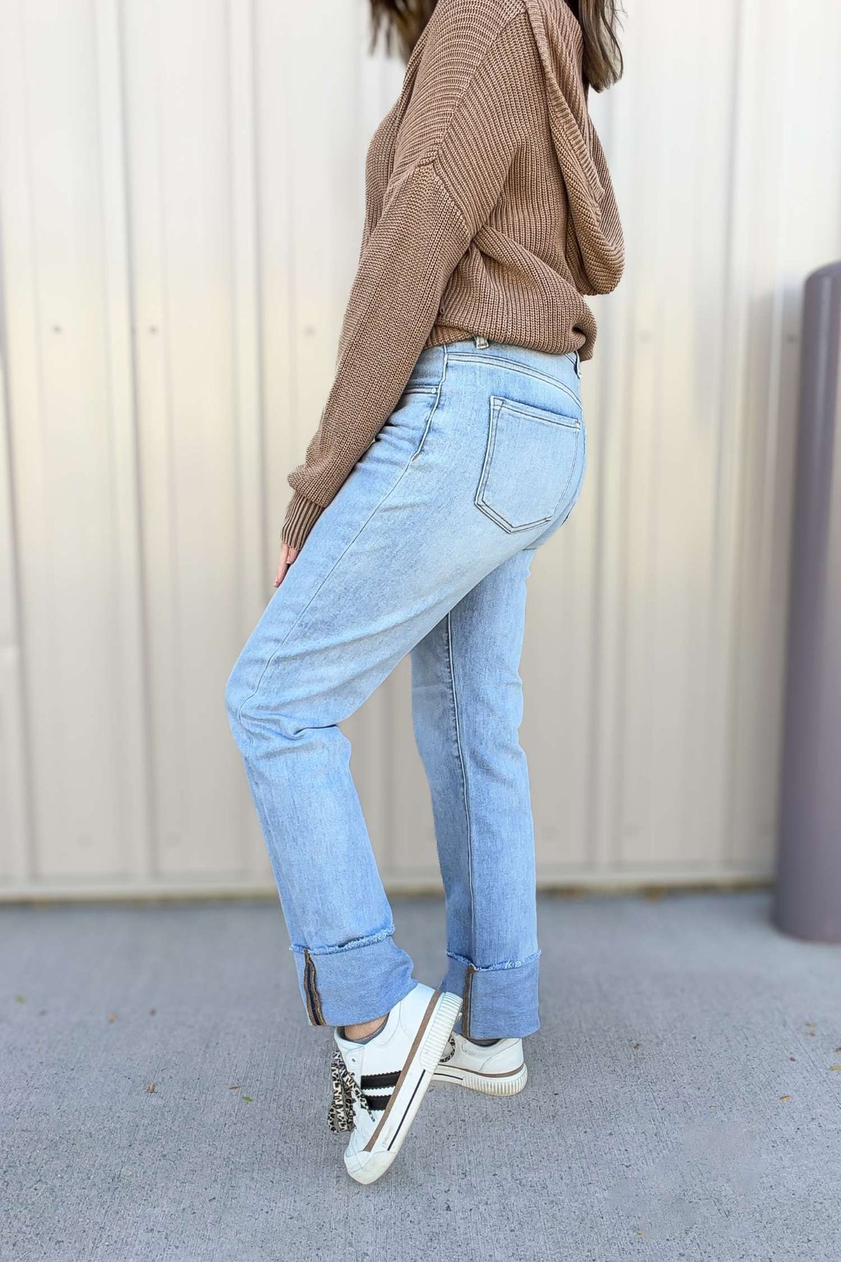 Person wearing light blue jeans and a brown sweater against a plain background