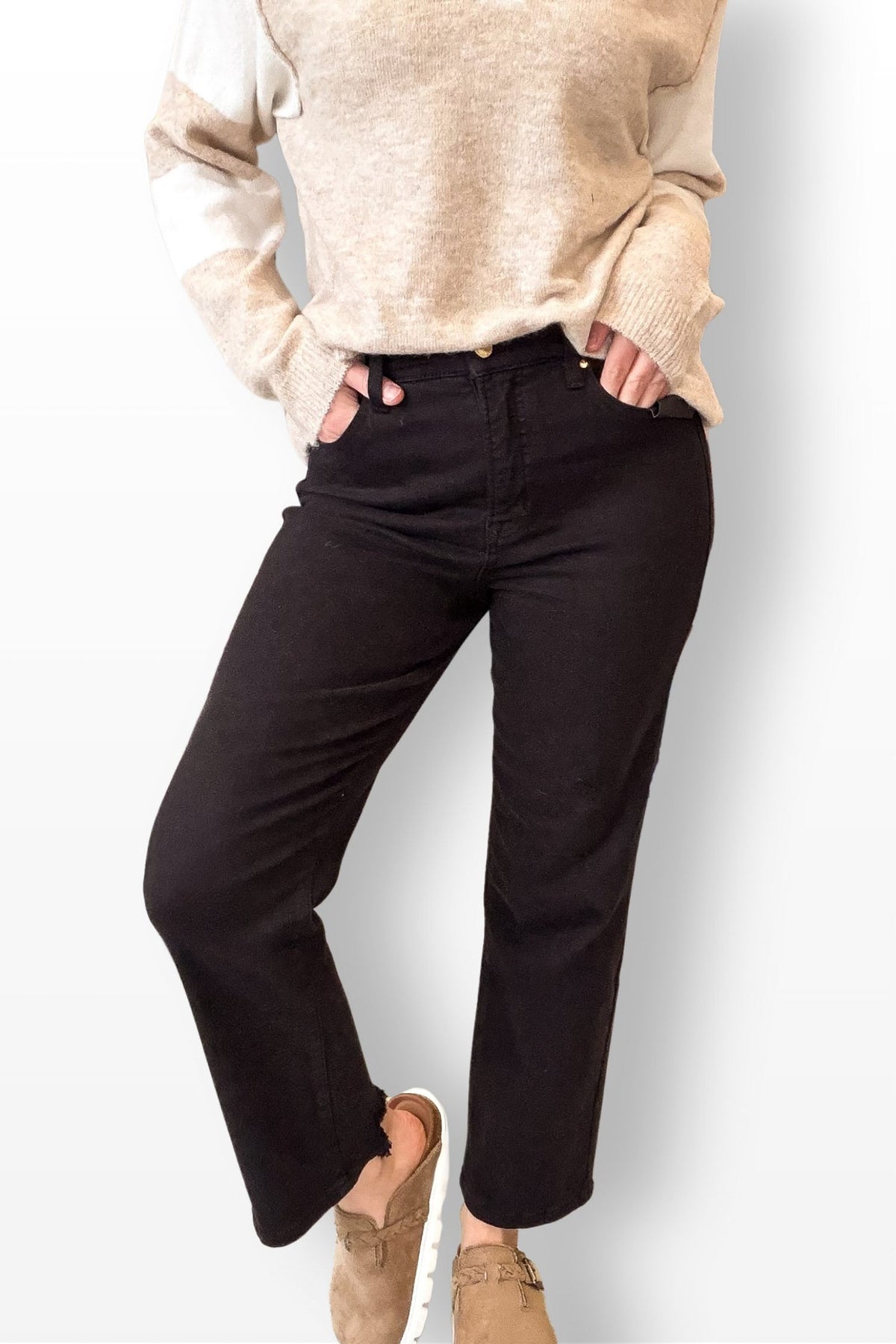 Person wearing a beige sweater and black pants on a white background