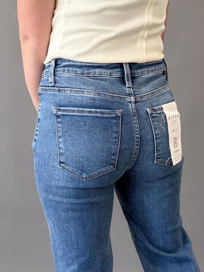 Person wearing blue risen jeans with a visible brand tag on a gray background