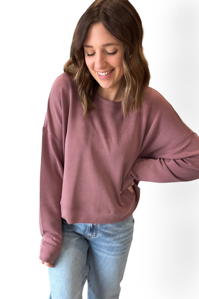 Woman wearing a Rose sweatshirt and light blue jeans on a white background