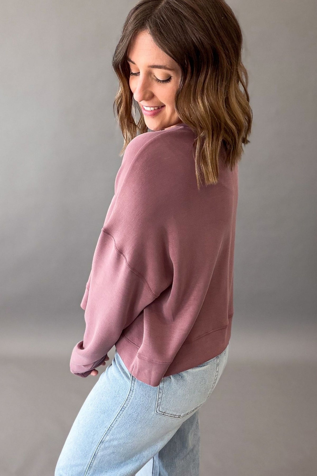 Woman wearing a rose drop shoulder sweatshirt and blue jeans showing back details