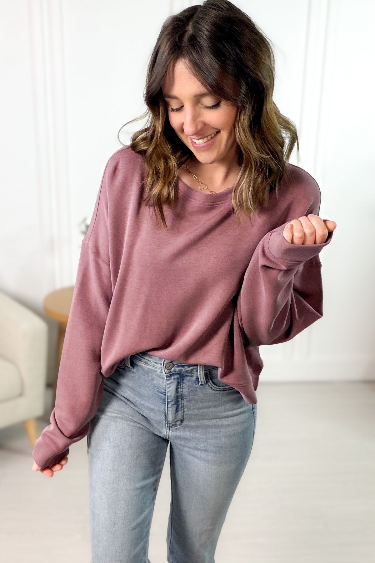 Woman wearing a rose sweatshirt and light blue jeans indoors.