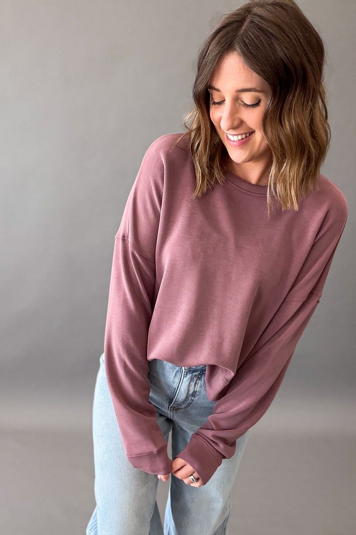 Woman wearing a rose drop shoulder sweatshirt and blue jeans